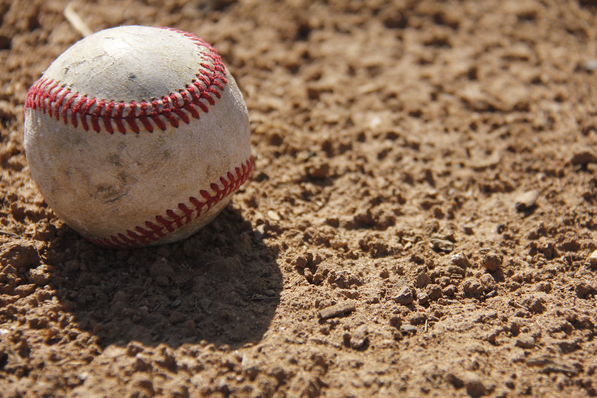 A worn baseball casting a shadow on infield dirt
