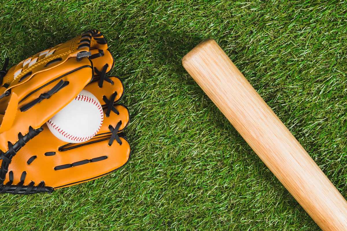 Top view of baseball bat with glove and ball on green grass