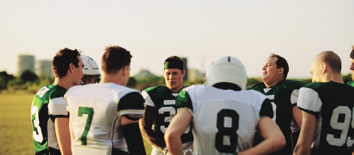 American football team standing in a huddle and talking strategy together during an afternoon practice