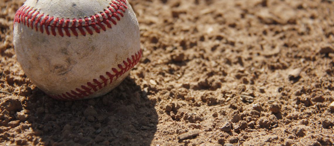 A worn baseball casting a shadow on infield dirt