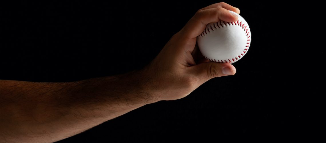 Baseball pitcher, close up of the hand ready to pitch on black background.