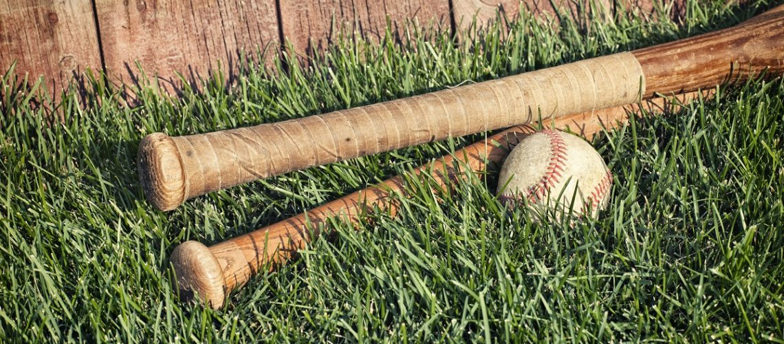 Vintage baseball and bats lying in grass in front of an old fence