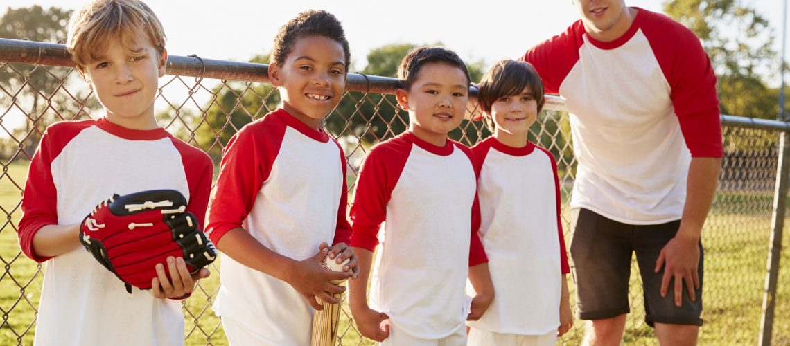 Coach and young boys in a baseball team looking to camera