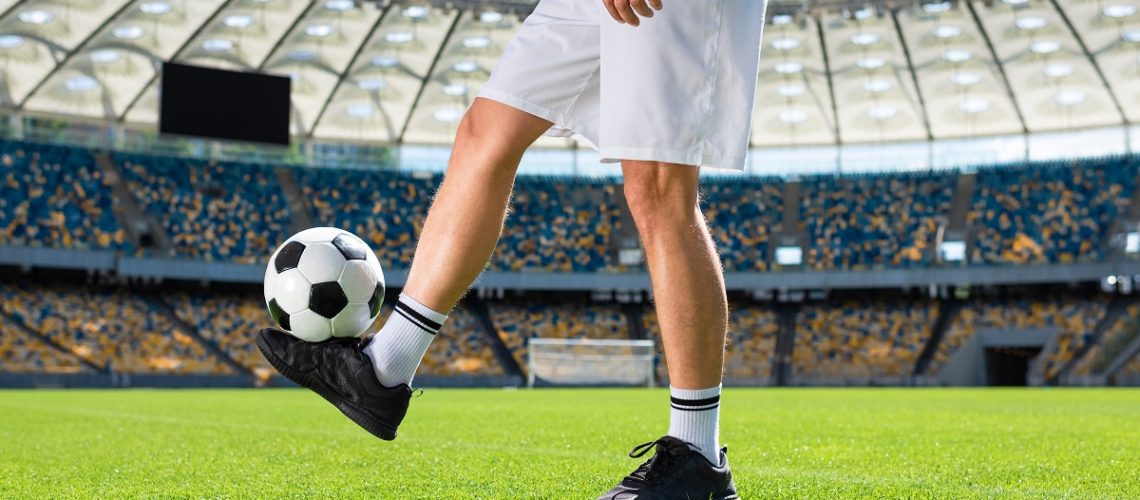 cropped shot of soccer player bouncing ball at sports stadium