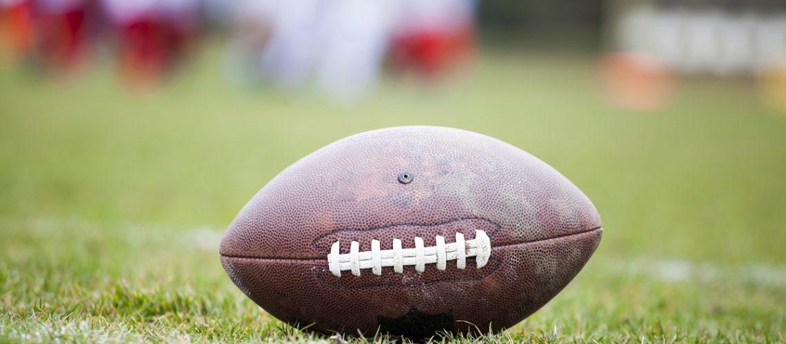 Close up of an american football on the field, players in the background