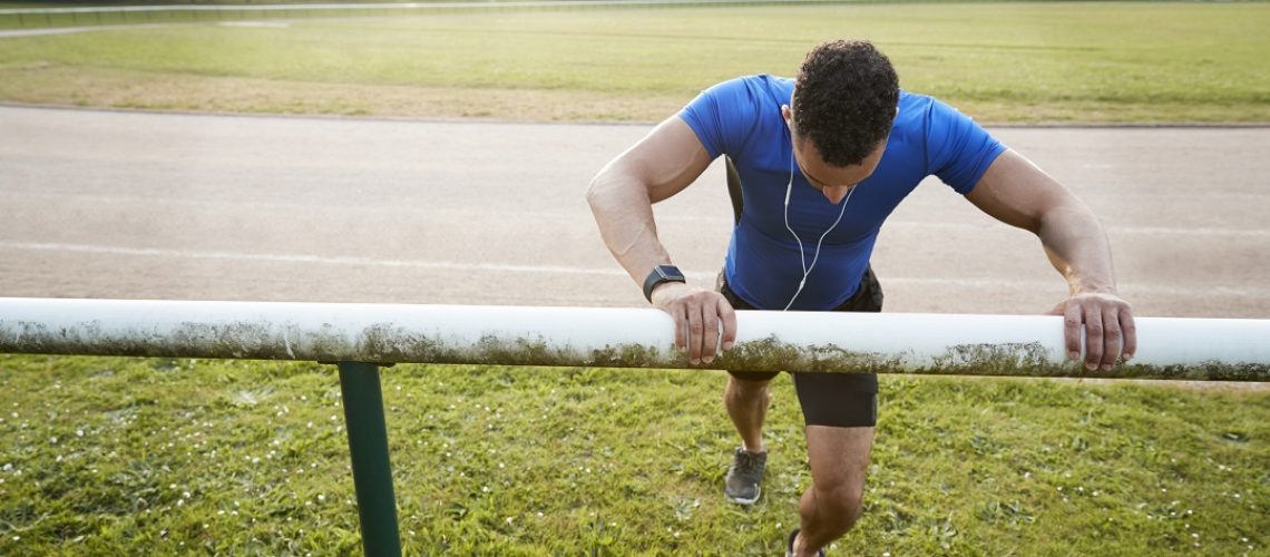 Male athlete stretching at running track, close up