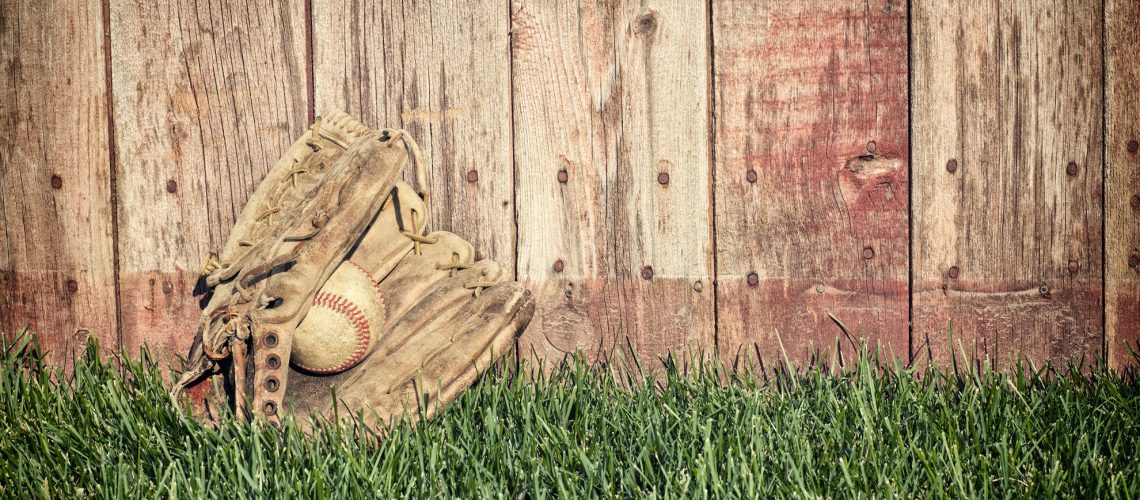 Old baseball mitt and ball on grass against wooden fence