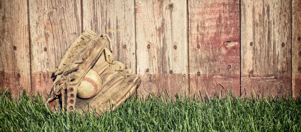 Old baseball mitt and ball on grass against wooden fence