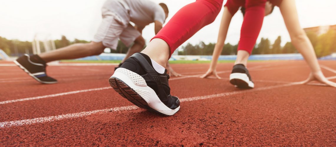 Low angle of sporty man and woman getting ready for sprint on stadium track