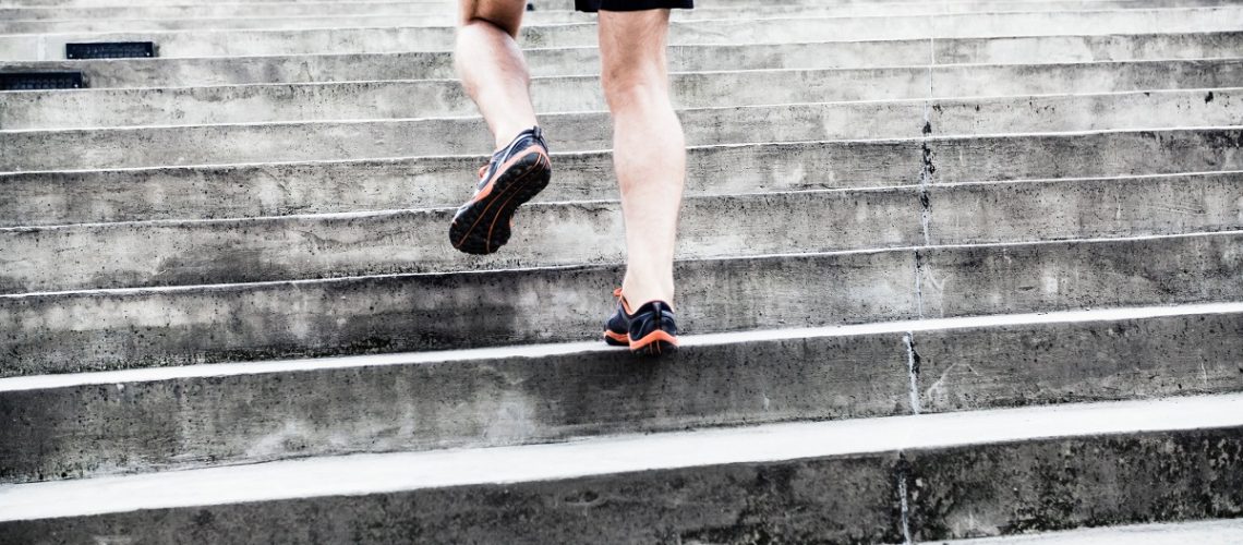 Man runner running on stairs in city. Young male athlete training and doing workout outdoors in city. Fitness, training and exercising outdoors in urban environment.
