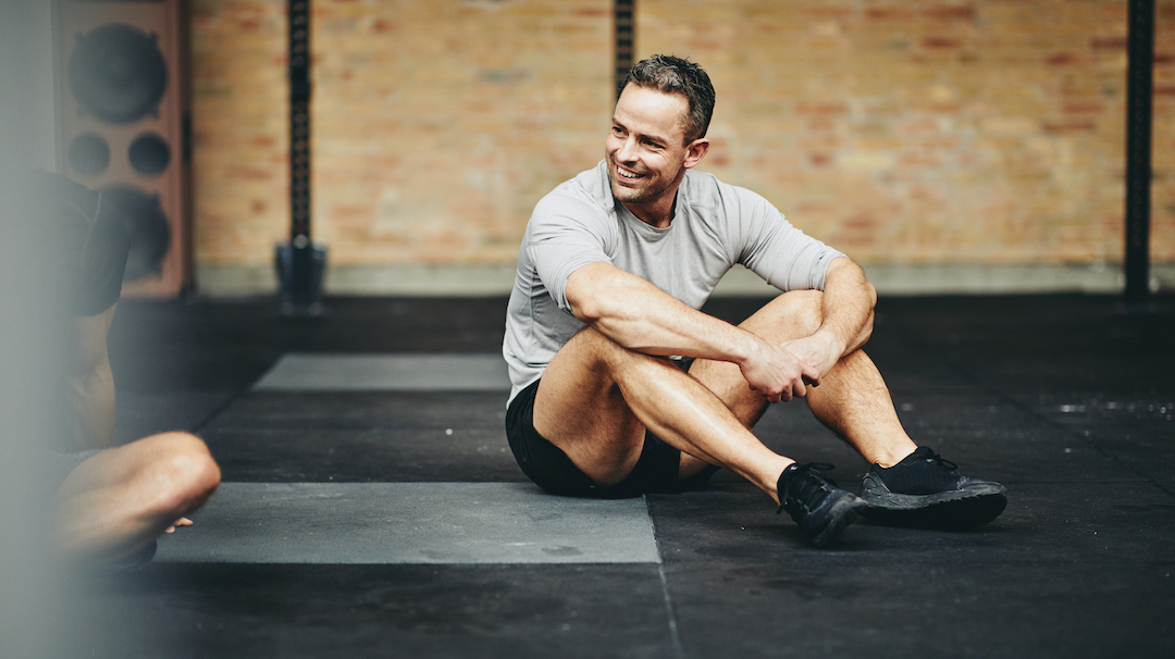 Smiling man sitting on a gym floor after working out